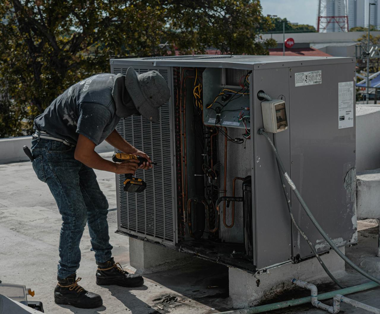NR Electric Job 3 A worker in a bucket hat repairs an outdoor air conditioning unit on a rooftop.